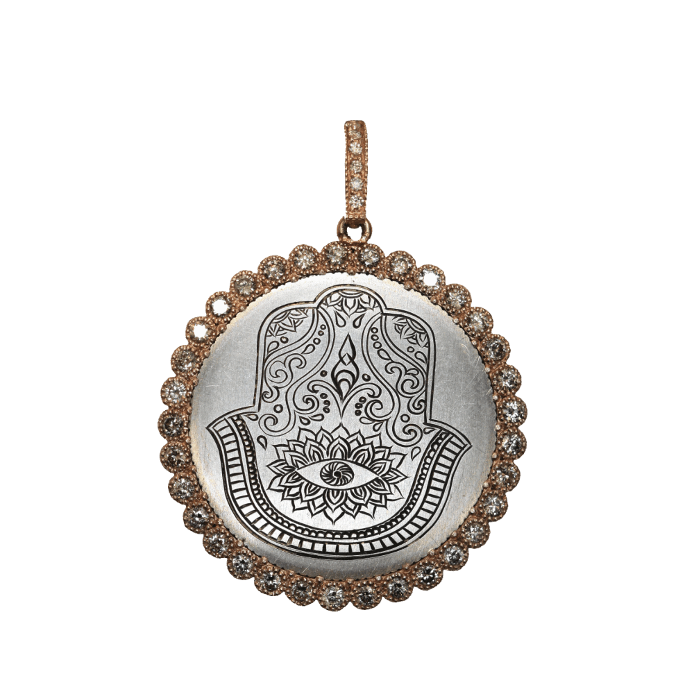 Cynthia Ann’s inspiration for her jewelry collection began as she was grieving the loss of her mother. Her spiritual journey led her to Europe where she started her precious collection of over 1,500 religious crosses and medals that date back to 450 A.D. through the early 1900’s. Cynthia Ann has “re-purposed” this Antique British Schilling with Hamsa Engraving for you to enjoy.
Antique British Schilling with Hamsa Engraving with Dot Bezel Made with Champagne Diamonds set in 14k Rose Gold, hanging from a champagne diamond and Rose Gold Openable Bale. Rose Gold Engraved Hamsa