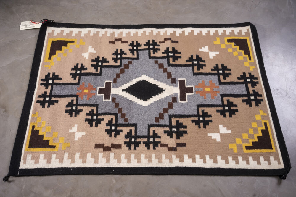 Part of Ken Johnson's collection of Navajo rugs, In the Style of Two Grey Hills features reddish tan ground and black border enclosing a bone patterned border and intricate grey, black, brown, red and orange design at center, surrounded by triangular black and orange designs at each corner. Rug Cn25 Two Grey Hills