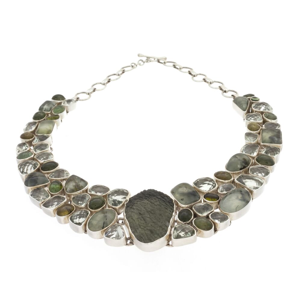This earthy tone Moldavite demi-collar includes many gemstones off-setting the unique texture of the cosmic-origin glass center. The assortment includes Green Tourmaline cabochons, Prehnite with Epidote cabochons and faceted Prasiolite all placed in a fluid sterling silver cagework setting with toggle clasp. Moldavite Necklace Collar With Prehnite & Epidote, Prasiolite And Tourmaline