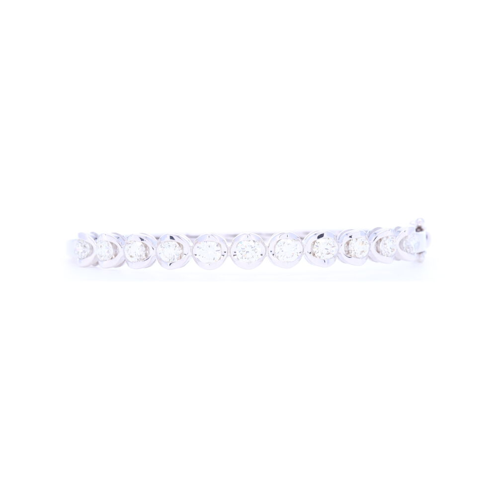This hinged bangle that has 2.1 carats of diamonds from 11 stones, is prong set with an 18k gold halo around each diamond. This bracelet is oval in shape so the pattern stays in front and it comfortably fits a wrist 6.5'' and smaller. 18k White Gold Prong Set Brilliant Cut Diamond Bangle